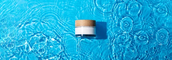 White cosmetic jar on the blue water surface. Blank label for branding mock-up. Summer water pool fresh concept. Flat lay, top view