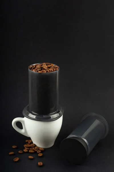 コーヒー豆とエアロプレスカップ 黒の背景に白いエスプレッソカップ エアロプレスはコーヒーを醸造するための装置です — ストック写真