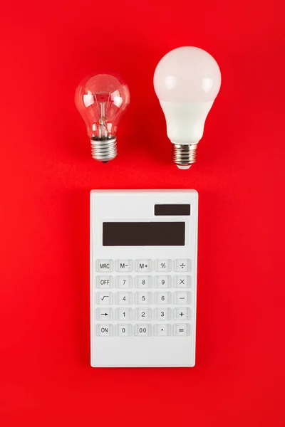 White calculator and incandescent lamp or LED bulb on red background. Concept showing the payment of electricity bills. The concept of savings electricity. Reducing the payment of utility bills