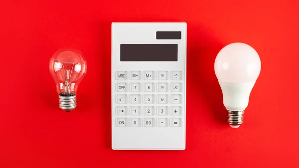 White calculator and incandescent lamp or LED bulb on red background. Concept showing the payment of electricity bills. The concept of savings electricity. Reducing the payment of utility bills