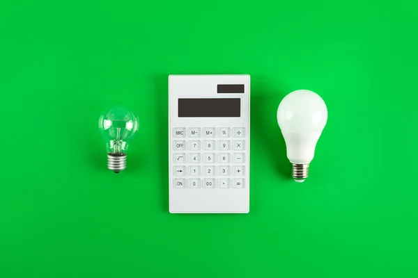 White calculator and incandescent lamp or LED bulb on green background. Concept showing the payment of electricity bills. The concept of savings electricity. Reducing the payment of utility bills