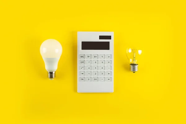 White calculator and incandescent lamp or LED bulb on yellow background. Concept showing the payment of electricity bills. The concept of savings electricity. Reducing the payment of utility bills