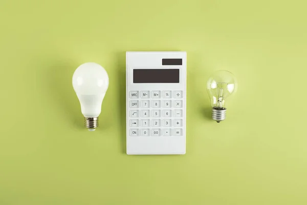Beyaz hesap makinesi ve parlak lamba ya da zeytin zemininde LED ampul. Elektrik faturalarının ödenmesi kavramı. Tasarruf elektriği kavramı. Faturaların ödenmesinde indirim