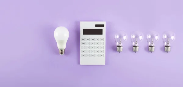 White calculator and incandescent lamp or LED bulb on purple background. Concept showing the payment of electricity bills. The concept of savings electricity. Reducing the payment of utility bills