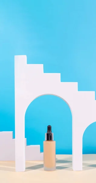 Liquid foundation cream with pipette unbranded bottle on blue background with arch, geometric figure. BB cream for professional make-up, eyedropper for applying to the face. Cosmetic female accessor