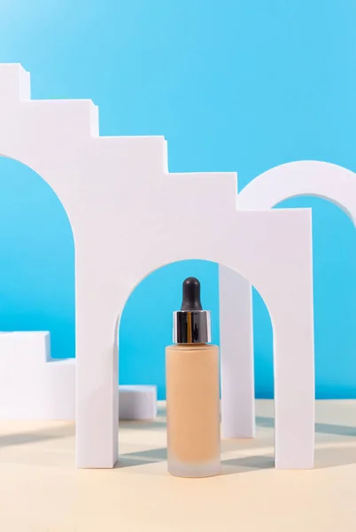 Liquid foundation cream with pipette unbranded bottle on blue background with arch, geometric figure. BB cream for professional make-up, eyedropper for applying to the face. Cosmetic female accessor