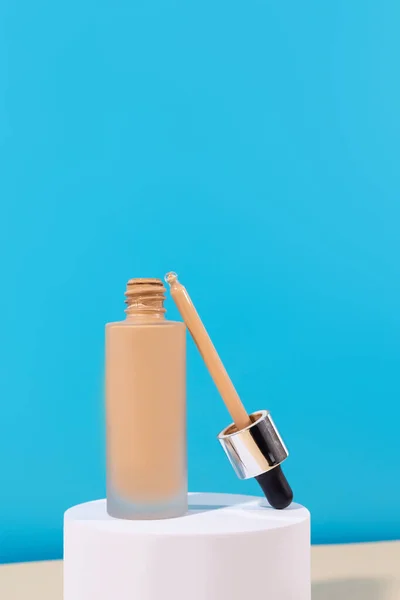 Opened liquid foundation cream with pipette unbranded bottle on a blue background. BB cream for professional make-up, eyedropper for applying to the face. Cosmetic female accessory, fluid. Mock u