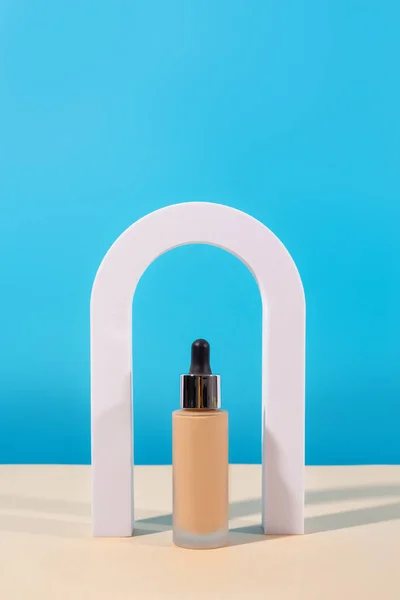 Liquid foundation cream with pipette unbranded bottle on blue background with arch. BB cream for professional make-up, eyedropper for applying to the face. Cosmetic female accessory, fluid. Mock u