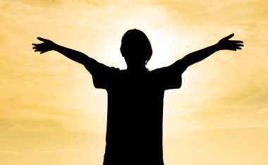 Akşamüstü güneş batana kadar kolları açık bir şekilde ayakta duran bir kadının silueti dinlenme gününde zihnini stresten arındırmak için bir siluet görüntüsü yaratır..