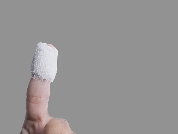 Yaralı bir parmağın yara enfeksiyonunu temizlemek ve önlemek için sargı beziyle tedavi edildiğini gösteriyor. Gri arkaplan ile izole görüntü. Kırpma yollarını kullan, kopyalama alanını kullanıma hazır et.