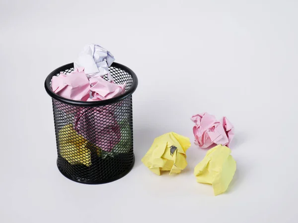 A small black basket made of round steel. Used to put garbage, documents that are not work and have been crushed so much that it overflows outside. In the white background there is copy space.