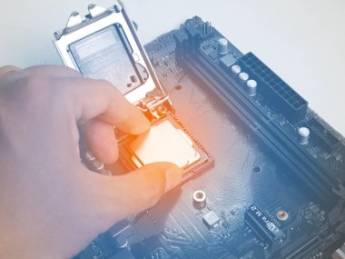 İşlemci kolunu tut ve ana karttaki işlemci yuvasına yerleştir. Eski bir anakart, çok tozlu. İşlemci yuvasına turuncu ışık koy. Yanında bir RAM yuvası var. Bir kapasitör var..