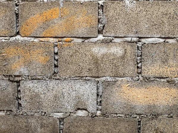 Bricks and blocks are laid together and connected by cement. It is a large wall with rough surface because the wall is not plastered to be smooth. old because of the sun and the rain