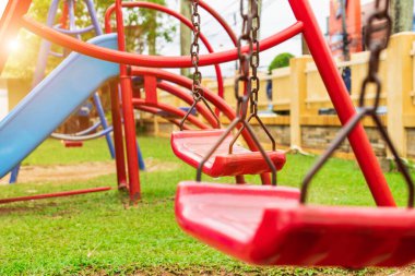 A red swing is attached to two old rusted chains in the playground. in the park saw the ground and the grass