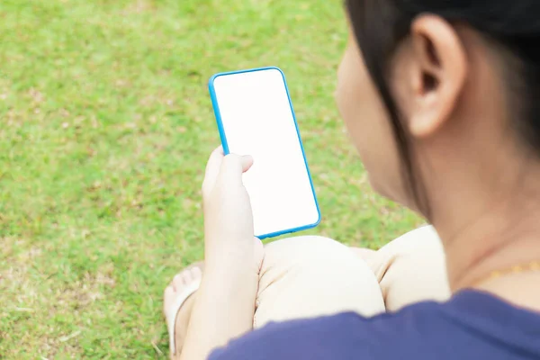 Taken from behind, across the shoulder of a blurry Asian woman. But clearly the mobile phone that cuts the screen to white Social media in the park