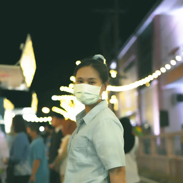 Maske takan Asyalı kadınlar gece düzenlenen bir etkinliğe giderler. Arka planda dairesel bir bokeh oluşturan birçok ampulle süslenmiştir..