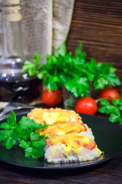 Sebze ve peynirle pişirilmiş balık, beyaz soslu, koyu arkaplanda.