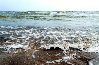 Sea waves and foam rolling onto the sandy shore. Cloudy weather at sea