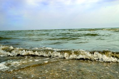 Sea waves and foam rolling onto the sandy shore. Cloudy weather at sea