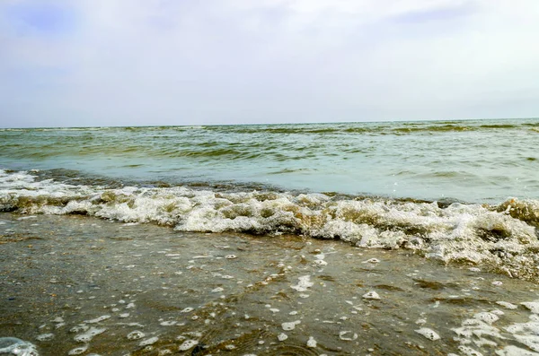 Sea waves and foam rolling onto the sandy shore. Cloudy weather at sea