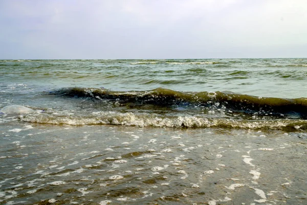 Sea waves and foam rolling onto the sandy shore. Cloudy weather at sea