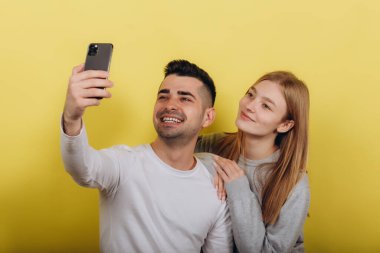 Mutlu heyecanlı genç seven Çift sarı duvar arka plan üzerinde izole ayakta fotoğrafını çekin bir selfie cep telefonuyla.