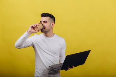 Sarı arka planda izole edilmiş beyaz ceketli gülümseyen genç adam, stüdyo portresi. İnsanların yaşam tarzı konsepti samimi duygular. Yerleşim kopyalama alanı. Elinde bir dizüstü bilgisayar tutuyor.