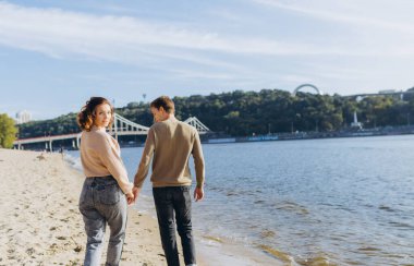 Mutlu romantik genç çift sahilde güzel bir gün batımı yürüyüşünün tadını çıkarıyor. Tatil yaşam tarzı kavramı