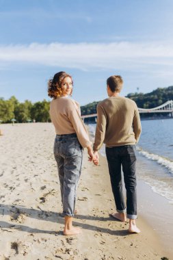 Mutlu romantik genç çift sahilde güzel bir gün batımı yürüyüşünün tadını çıkarıyor. Tatil yaşam tarzı kavramı