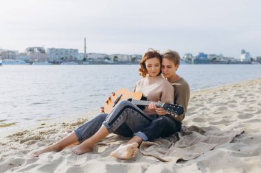 Sahilde erkek öğretmenden gitar öğrenen genç bir kız. Gitar akorları gösteriliyor.