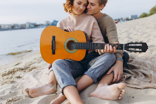 young guy teaching his girlfriend how to play guitar, self-taught. Couple in love having fun on the beach hugging and kissing