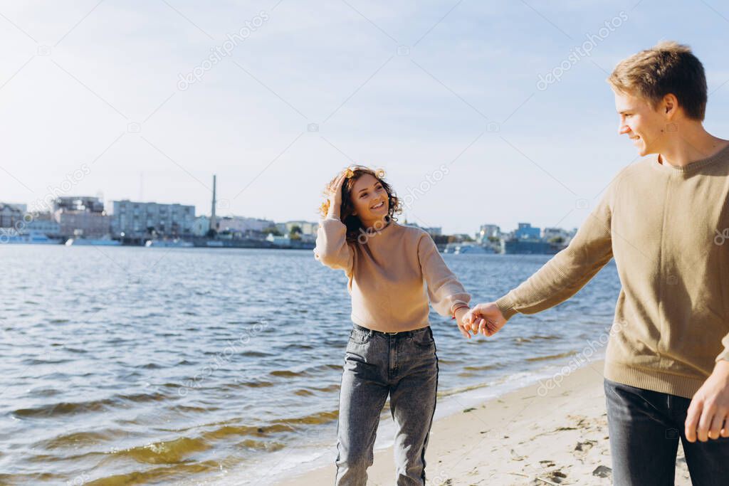 two young people in love running on the beach. They smile at each other. Beautiful couple. Beach. Feeling. Dress in a sweater