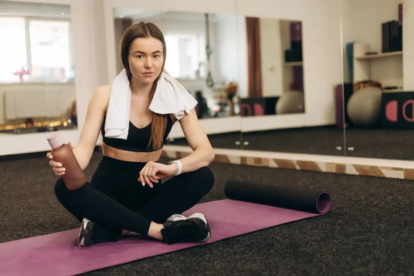 Antrenmandan sonra paspasın üzerinde oturan güzel kız. Kız gülümsüyor. Sağlıklı yaşam tarzı kavramı. Fitness