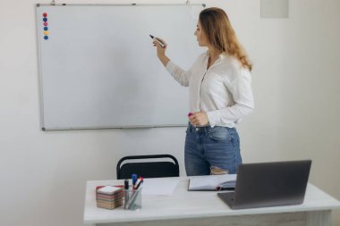 Genç kız öğretmen öğrenciler için bir tahtaya yazı yazar. Online eğitim. Giyin.