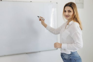 Genç kız öğretmen öğrenciler için bir tahtaya yazı yazar. Online eğitim. Giyin.