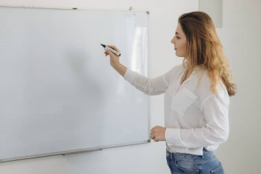 Genç kız öğretmen öğrenciler için bir tahtaya yazı yazar. Online eğitim. Giyin.