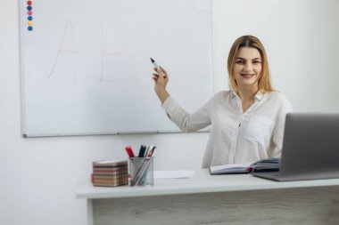 E-öğrenme. Genç öğretmen kız sınıfta dizüstü bilgisayarın önünde oturuyor ve görüntülü sohbet yoluyla online ders veriyor. Uzaktan eğitim kavramı.
