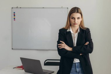 Tatmin olmamış bir öğretmenin portresi. Ellerini kemerinde tutuyor. Kız beyaz gömlek ve siyah ceket giyiyor.