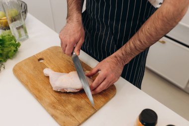 Mutfak masasında yemek pişirmek için ürünler. Bir adam tahtada tavuk kesiyor.