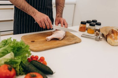 Mutfak masasında yemek pişirmek için ürünler. Bir adam tahtada tavuk kesiyor.