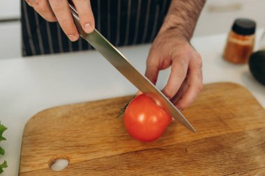Adamın biri tahtada kırmızı domates kesiyor.