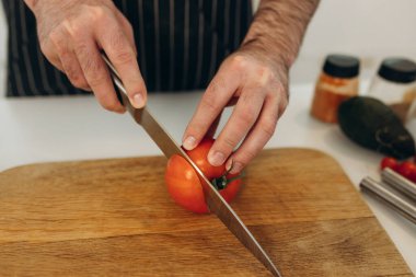 Adamın biri tahtada kırmızı domates kesiyor.