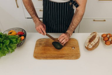 Adamın biri mutfak masasında avokado kesiyor.