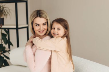 Anne ve küçük kızın yakın plan portresi. Kız gülümsüyor ve annesine sarılıyor.