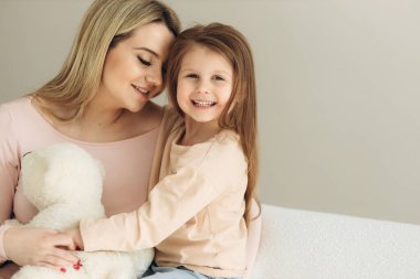 Anne ve küçük kızın yakın plan portresi. Kız gülümsüyor ve annesine sarılıyor.