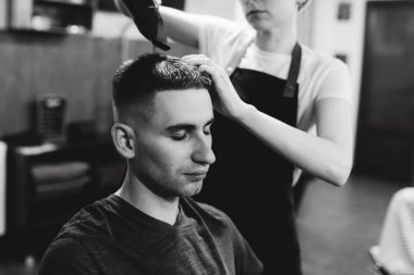 Şimdiden iyi görünüyorsun. Berber dükkanında saç kurutma makineli bir kuaför tarafından tımar edilen genç adamı yakından izle.