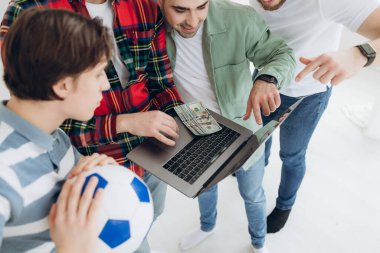 Bir grup erkek arkadaş dizüstü bilgisayardan spor bahis kuponlarına bakıyor. Hangi takıma oynayacağına karar ver. Kumar konsepti. Spor bahisleri. Online bahis