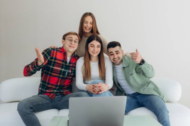 Kanepede oturup internetten video izleyen ya da dizüstü bilgisayardaki sosyal ağ uygulamasını kullanan bir grup arkadaş.