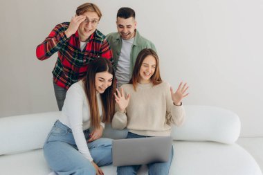 Kanepede oturup internetten video izleyen ya da dizüstü bilgisayardaki sosyal ağ uygulamasını kullanan bir grup arkadaş.