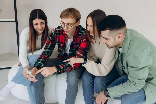 Neşeli adam, arkadaşlarıyla birlikte oturup gülerken cep telefonunda bir video gösteriyor. Bir grup neşeli genç adam ve kadın evlerinde akıllı telefona bakıp gülüyorlar..